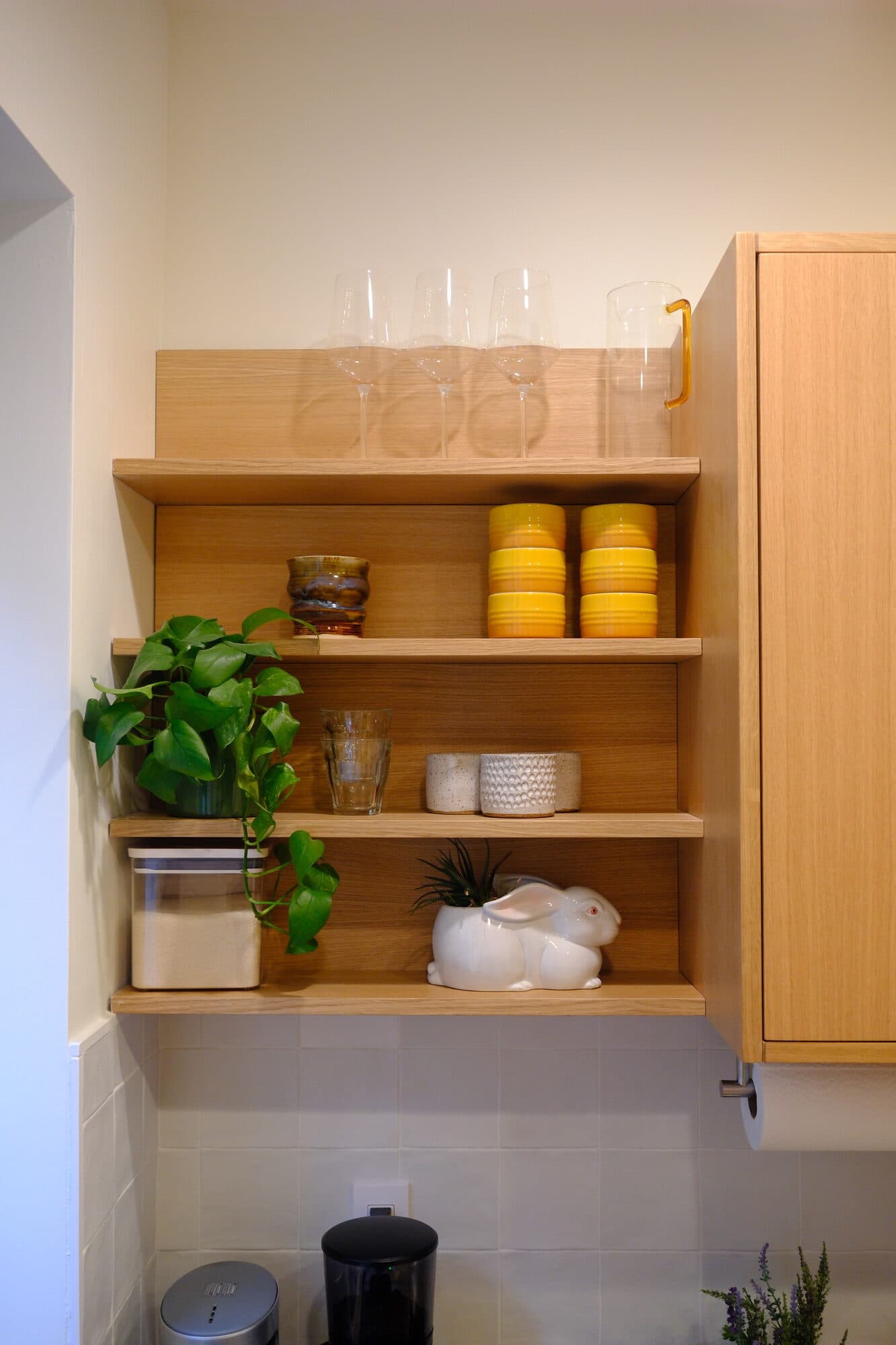 Open oak shelving styled with dishes and plants against white tile